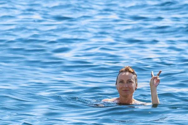 woman swims in the sea and shows hand victory sign on a clear summer day