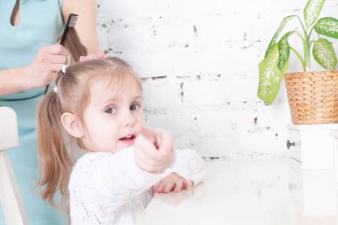 Annenin elleri beyaz elbiseli, gülümseyen bir kızı tarıyor.