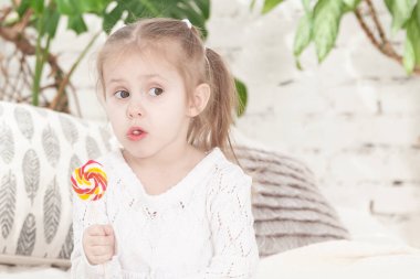 Üç yaşındaki gülümseyen küçük bir kızın portresi şeker yiyor.