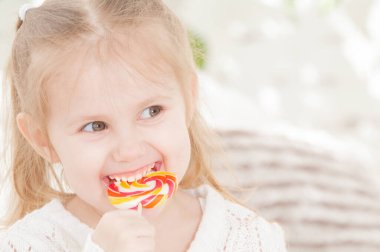 Üç yaşındaki gülümseyen küçük bir kızın portresi şeker yiyor.