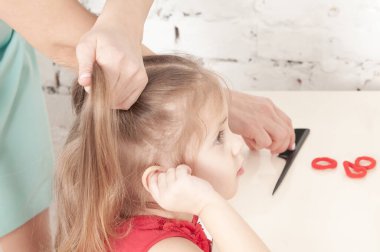 Annenin elleri kırmızı elbiseli, gülümseyen bir kızı tarıyor.