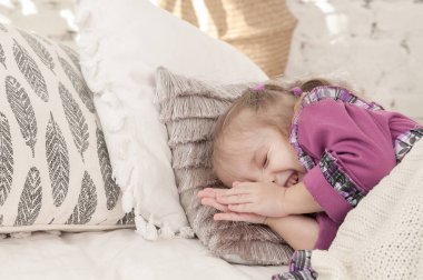 Üç yaşındaki küçük bir kız yatakta uzanıyor ve neşeyle uyumaya çalışıyor.