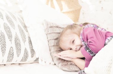 Üç yaşındaki küçük bir kız yatakta uzanıyor ve neşeyle uyumaya çalışıyor.