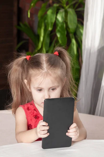Маленькая Девочка Красном Платье Сидит Столом Играет Планшетом Задумчивым Взглядом — стоковое фото