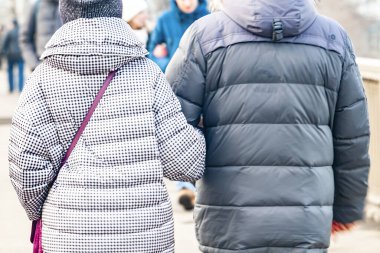 Bir çift insan, açık bir günde el ele yürürken, arkadan bakıyorlar.