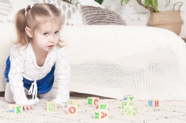 3 yaşındaki küçük bir kız yatağın yanına harflerin ve numaraların çizildiği küplerle oynar.