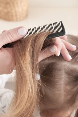 Annenin elleri kırmızı elbiseli, gülümseyen bir kızı tarıyor.