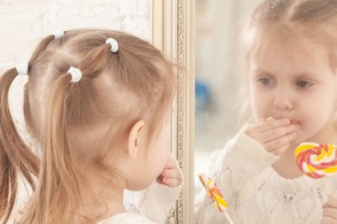 Üç yaşındaki gülümseyen küçük bir kızın portresi şeker yiyor.