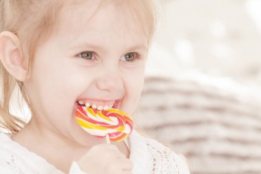 Üç yaşındaki gülümseyen küçük bir kızın portresi şeker yiyor.