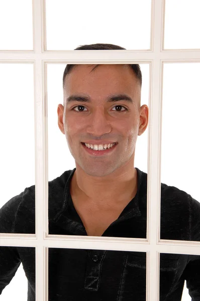 Junger Mann lächelt hinter weißem Fensterrahmen — Stockfoto