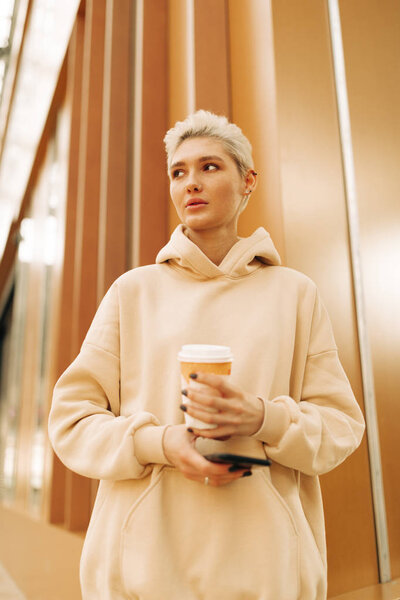 Настоящая молодая женщина с чаем и мобильным телефоном
