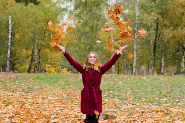 Hermosa mujer en un parque abrigo hojas de otoño volar —  Fotos de Stock