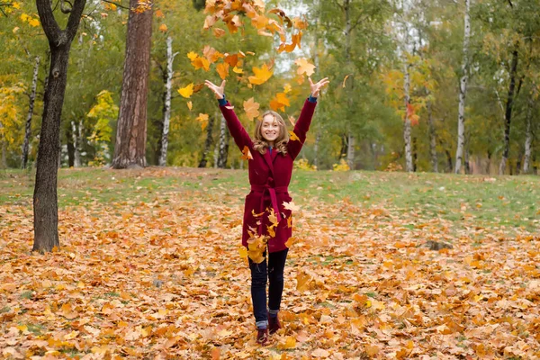 Hermosa mujer en un parque abrigo hojas de otoño volar —  Fotos de Stock