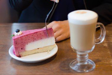 Genç güzel kadın tablo kek üzerine köpük sütlü kahve içer