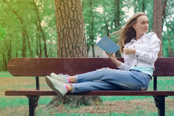 Mulher bonita em um banco de natureza lendo um livro — Fotografia de Stock