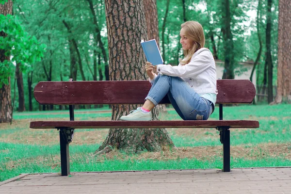 Mulher bonita em um banco de natureza lendo um livro — Fotografia de Stock