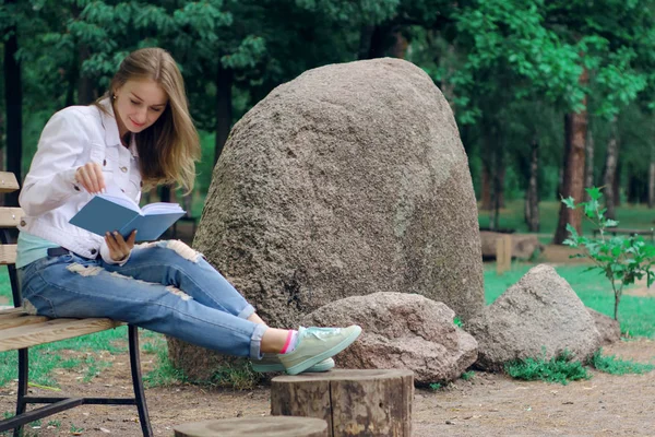 Mulher bonita em um banco de natureza lendo um livro — Fotografia de Stock