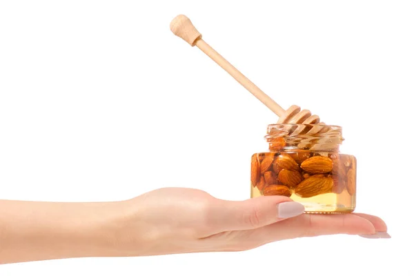 Um pote de mel com uma colher de mel nozes amêndoas nas mãos — Fotografia de Stock