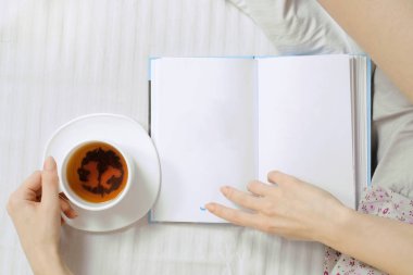 Güzel genç kadın yatakta kitap okuma çay içme