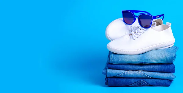 Στοίβα διπλωμένα τζιν και γυαλιά ηλίου, λευκά αθλητικά παπούτσια — Φωτογραφία Αρχείου