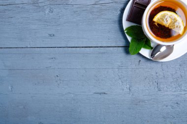 Mavi gri ahşap arka planda limon ve çikolatalı beyaz nane çayı.