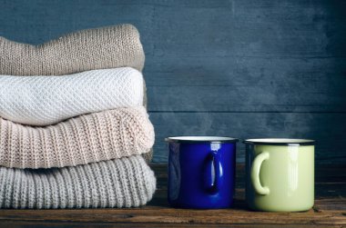 Örgü örülmüş kalın giysiler ve fincanlar ahşap arka planda çay, kazaklar, örgü giysiler yığını.