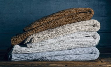 Ahşap arka planda örülmüş kalın giysiler, kazaklar, örgü giysiler yığını.