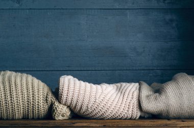 Ahşap arka planda örülmüş kalın giysiler, kazaklar, örgü giysiler yığını.