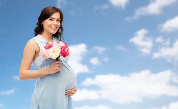Šťastná těhotná žena s květinami přes modrou oblohu — Stock fotografie