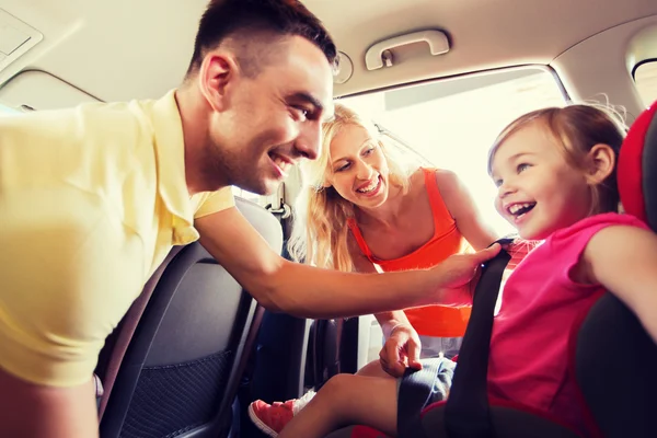 Feliz padres abrochando niño con cinturón de seguridad de coche — Foto de Stock