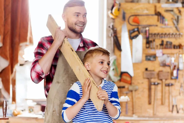 Feliz padre e hijo con tabla de madera en el taller —  Fotos de Stock