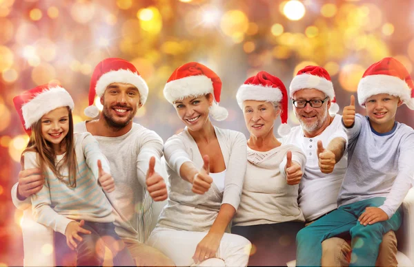 Happy family in santa hats showing thumbs up — Stock Photo, Image