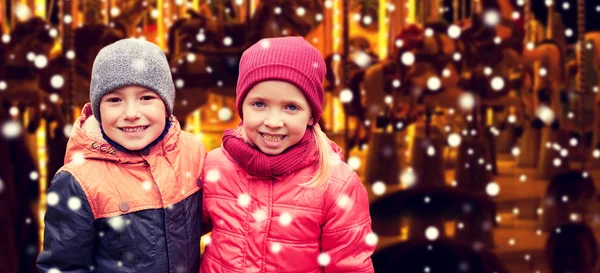 Little girl hugging boy over snow and carousel — Stockfoto