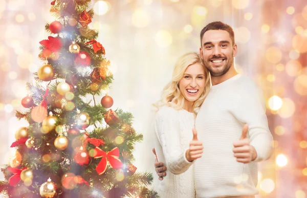 Happy couple showing thumbs up with christmas tree — Stock Photo, Image