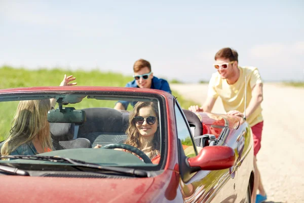 Amigos felizes empurrando carro cabriolet quebrado — Fotografia de Stock