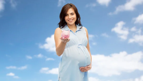 Gelukkig zwangere vrouw met spaarpot over blauwe hemel — Stockfoto