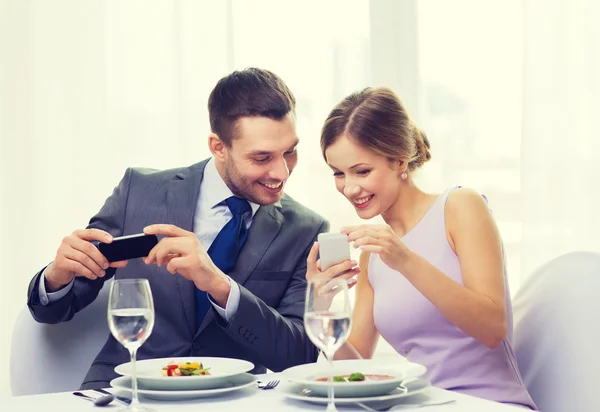Couple souriant avec amuse-gueule et smartphones — Photo