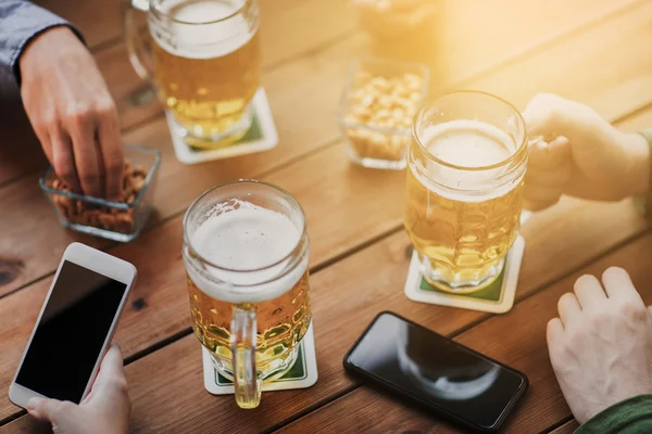 Close up of hands with smartphones and beer at bar — Stock Photo, Image