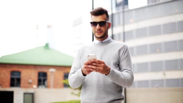Людина в сонцезахисних окулярах зі смартфоном на міській вулиці — стокове відео
