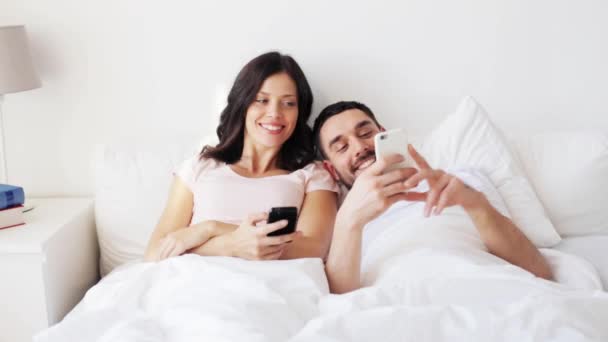 Pareja feliz con smartphones en la cama — Vídeo de stock