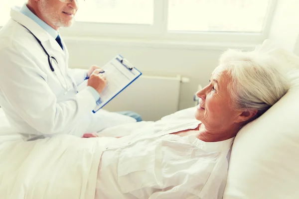 Senior woman and doctor with clipboard at hospital — Stock Photo, Image
