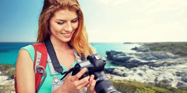 Happy woman with backpack and camera over seashore — Stock fotografie