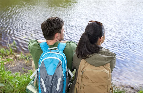 Пара с рюкзаками сидят на берегу реки — стоковое фото