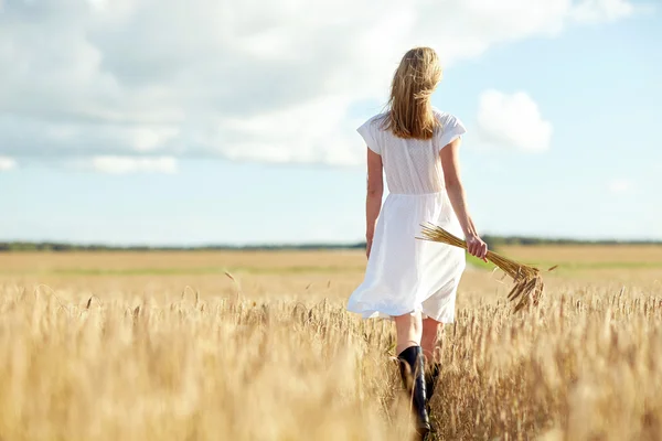 Mujer joven con espiguillas de cereales caminando en el campo — Foto de Stock