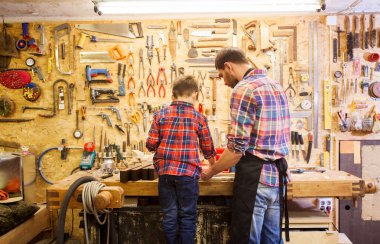 father and little son with wood plank at workshop clipart
