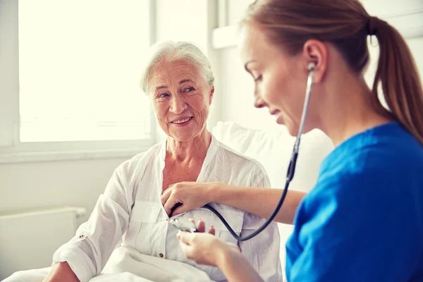 Sygeplejerske med stetoskop og senior kvinde på klinikken - Stock-foto