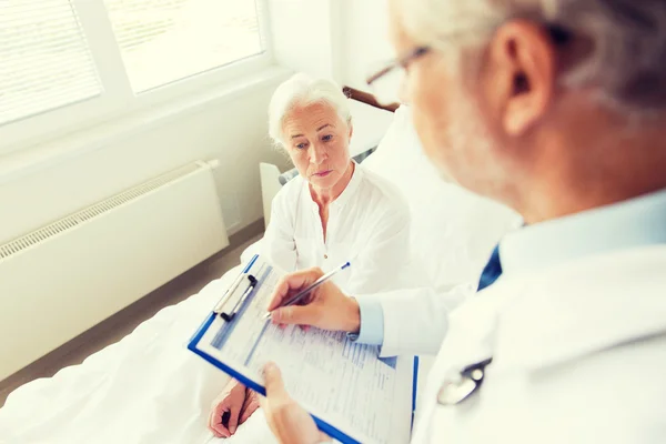 Senior woman and doctor with clipboard at hospital — Stock Photo, Image