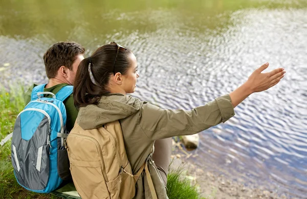 Echtpaar met rugzakken zittend op de rivier bank — Stockfoto