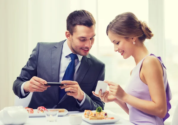 Pareja sonriente con sushi y smartphones — Foto de Stock