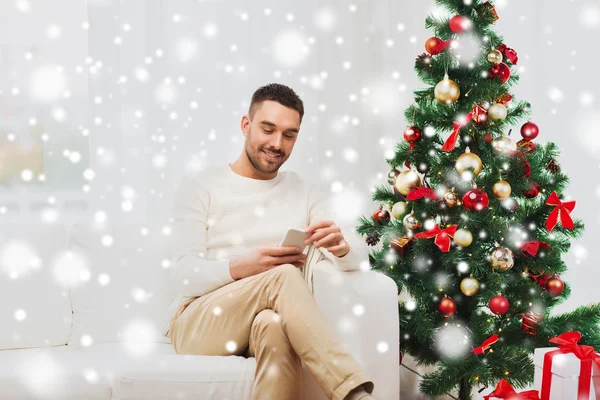 Lächelnder Mann mit Smartphone zu Weihnachten zu Hause — Stockfoto